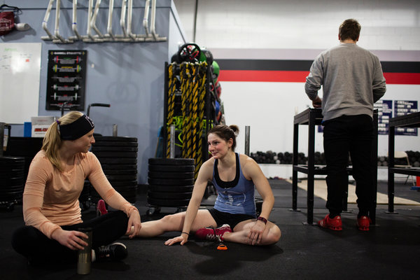 Alex Larcom, left, and Ali Huberlie stretching together at CrossFit Boston. Both women met their partners through the CrossFit community. Photo from New York Times 